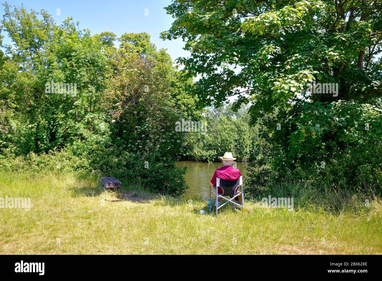 Ein eleganter und gut gekleideter älterer Herr, der an einem heißen Sommertag in Surrey England auf einem Sitz an der Themse in Runnymede sitzt Stockfoto