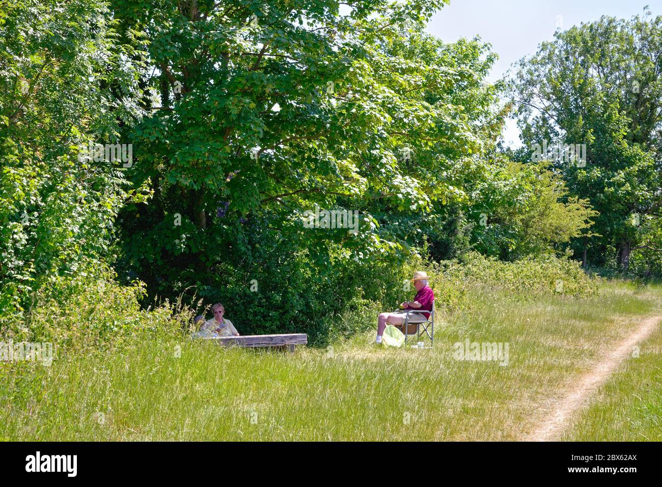 Ein eleganter und gut gekleideter älterer Herr, der an einem heißen Sommertag in Surrey England auf einem Sitz an der Themse in Runnymede sitzt Stockfoto