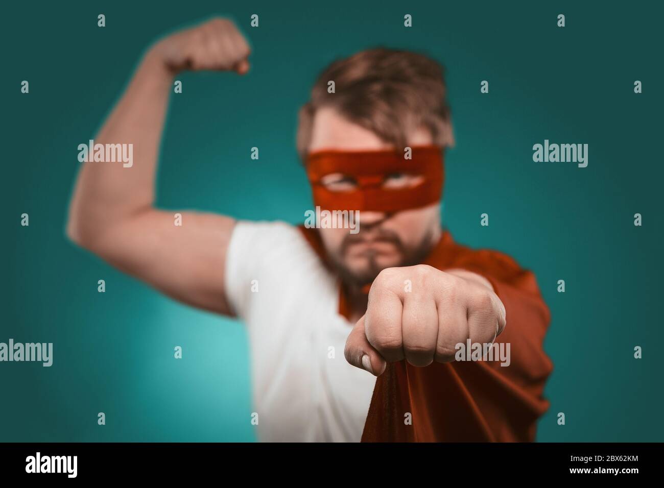 Mutiger Superhelden-Mann zeigt Muskeln beim Betrachten der Kamera. Attraktive kaukasischen Kerl in roter Maske und Mantel bereit, die Welt zu retten. Konzentrieren Sie sich auf die Faust Stockfoto