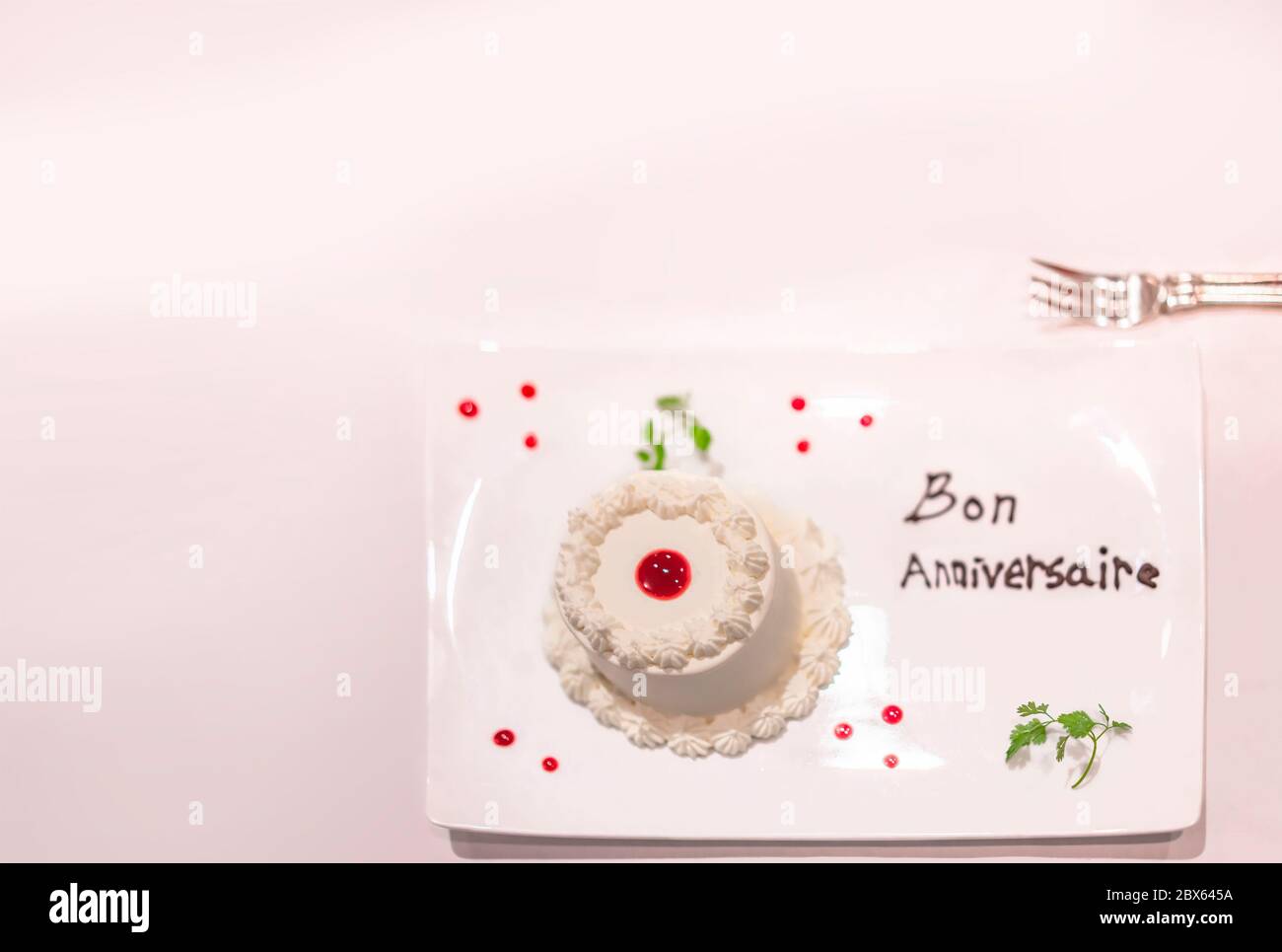 Kleiner weißer Kuchen auf einem Teller mit Erdbeersauce und Minzblättern  mit Happy Birthday oder Bon Anniversaire in französisch in chocol  Stockfotografie - Alamy