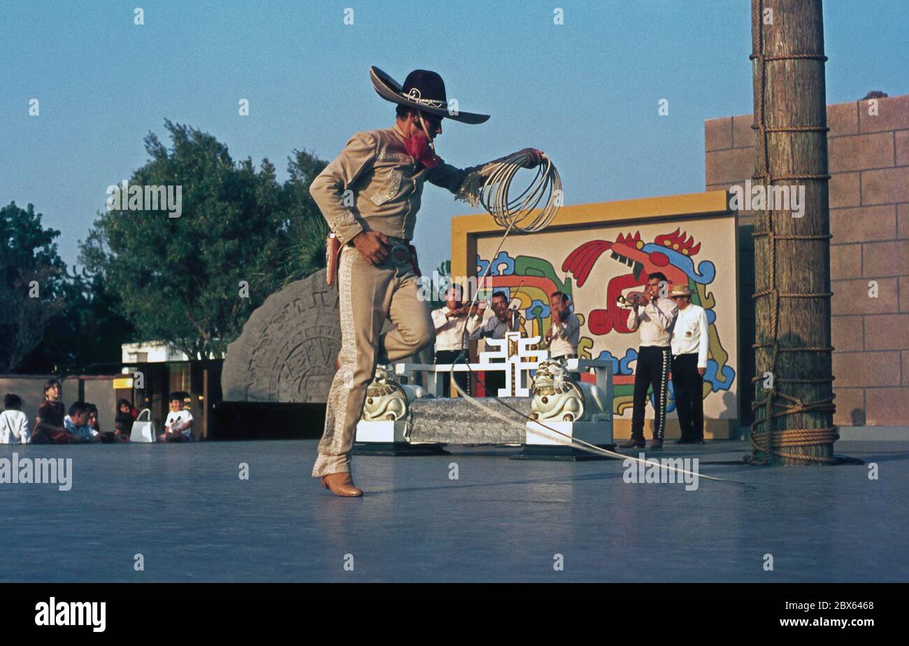 Ein Mann, der Tricks auf der Bühne mit einem Lasso begleitet von einer Blaskapelle, USA in den 1950er Jahren. ‘dträgt traditionelle mexikanische Cowboy (Gaucho) Kleidung, während er in und aus dem Seil tanzt. Er kommt aus der Chicano-Gemeinschaft in den USA – Männer und Frauen mexikanischer Abstammung. Stockfoto