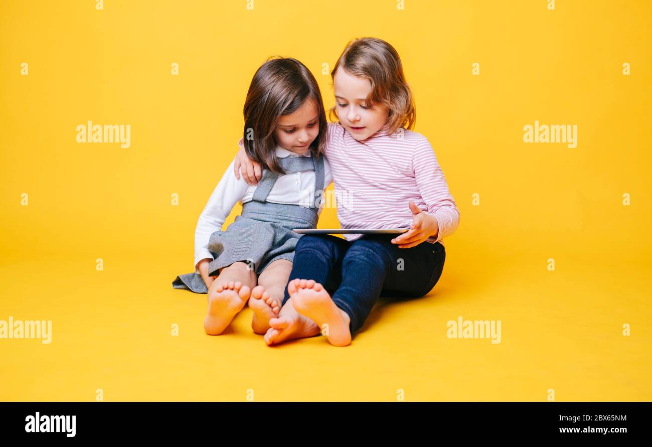 Zwei Mädchen verwenden ein digitales Tablet auf gelbem Hintergrund Stockfoto