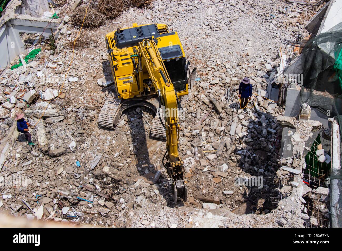 Der Tieflöffel Maschinen arbeiten vor Ort Abriss eines alten Gebäudes Arbeiter Spritzwasser, Staub zu erhalten. Stockfoto