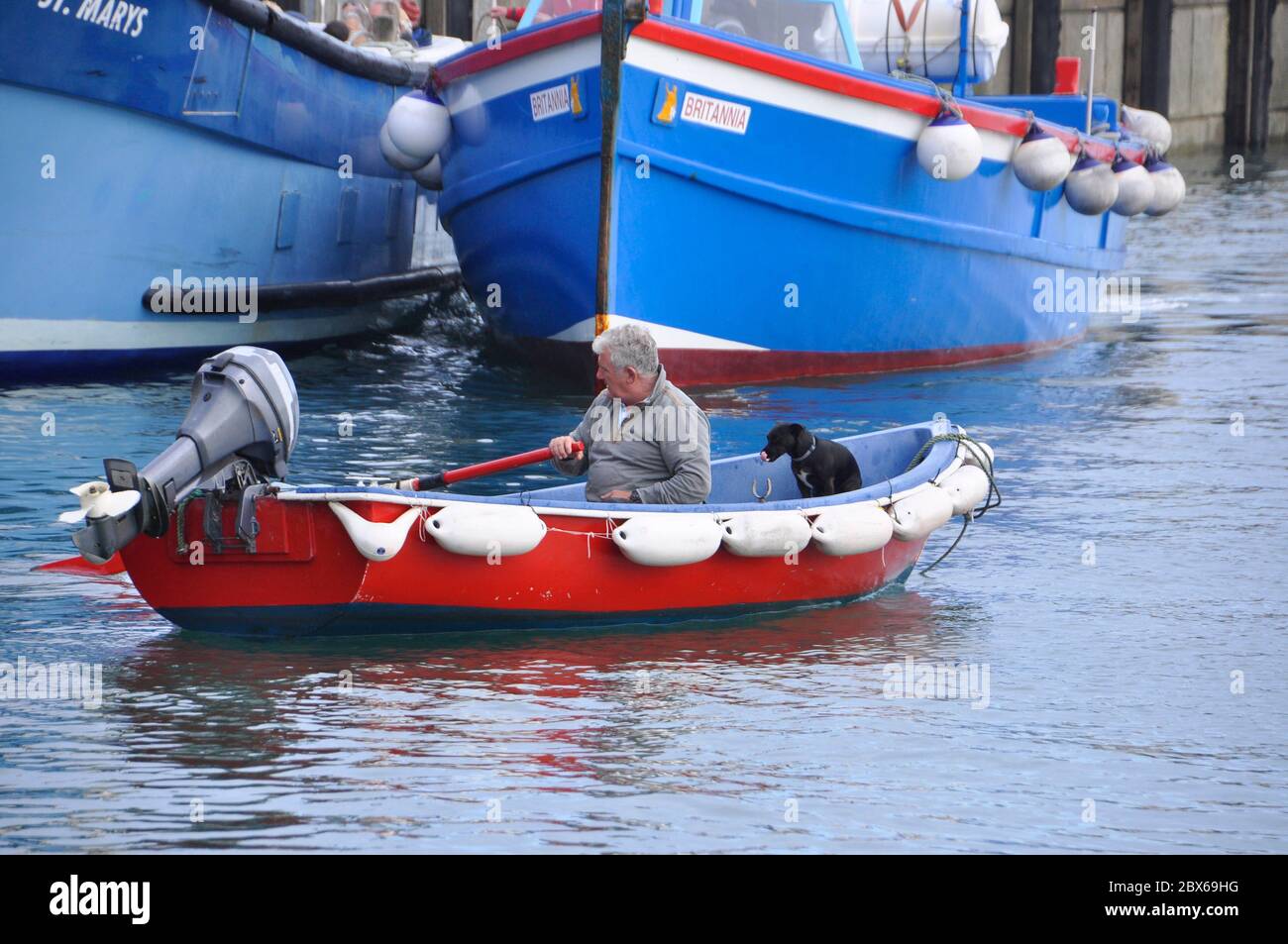 Einer der Scilly-Bootsmänner reiht sich mit seinem Hund zu seinem Boot aus, um seinen Tag zu beginnen und Touristen zwischen und um die Inseln zu befördern. St. Mary's Harb Stockfoto