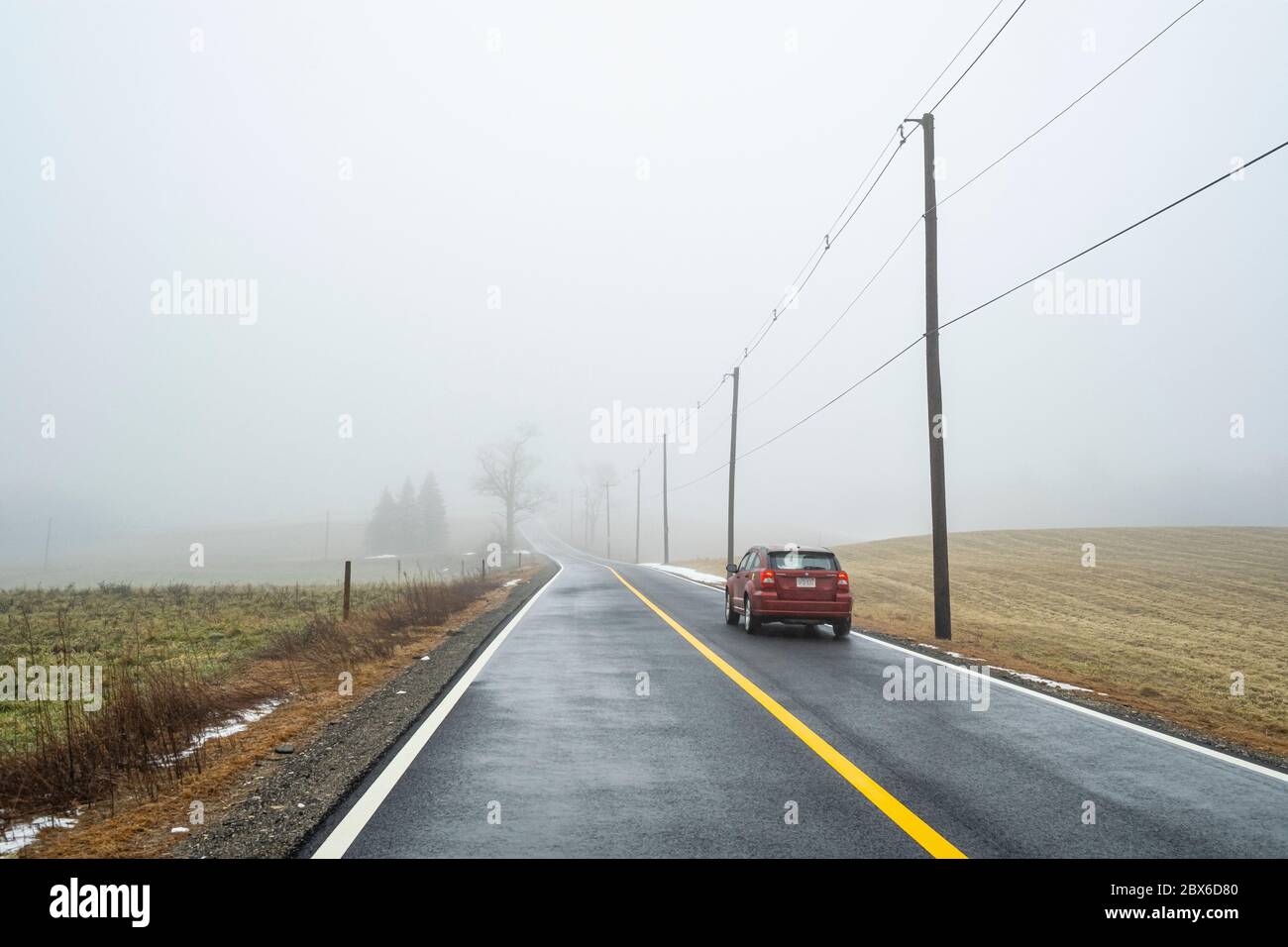 Ein rotes Auto fährt eine einsame Straße hinunter Stockfoto