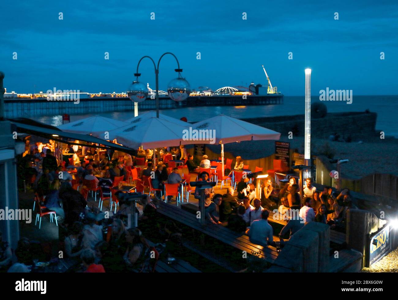 Eine Strandbar mit dem Palace Pier. Die Stadt West Sussex Brighton am Meer. Die Bars, Clubs und das Nachtleben machen die Stadt zu einem beliebten Reiseziel Stockfoto