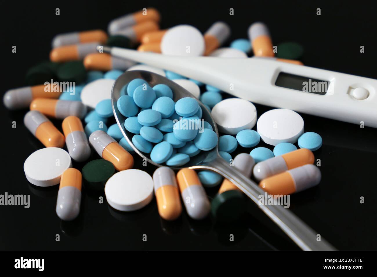 Pillen in Löffel und Digitalthermometer ein dunkler Glastisch. Konzept der fiebersenkenden Medikamente, Antibiotika, Vitamine Stockfoto