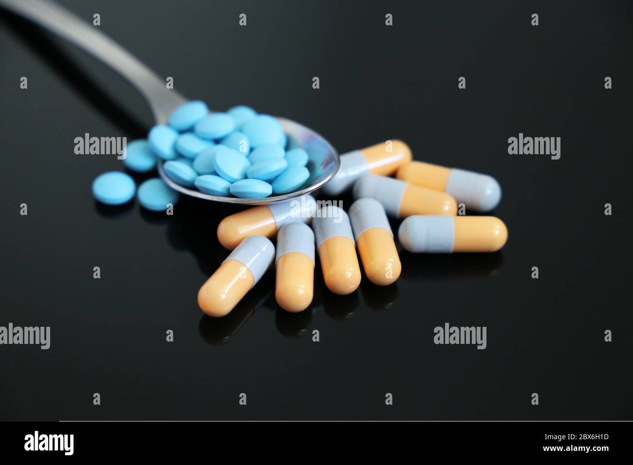 Löffel mit Pillen, Medikamente in Kapseln und Tabletten auf einem dunklen Glastisch. Konzept der Apotheke, Antibiotika, Vitamine Stockfoto