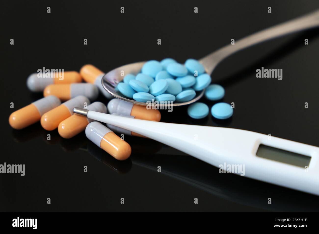 Pillen in Löffel und Digitalthermometer ein dunkler Glastisch. Konzept der fiebersenkenden Medikamente, Antibiotika, Vitamine Stockfoto