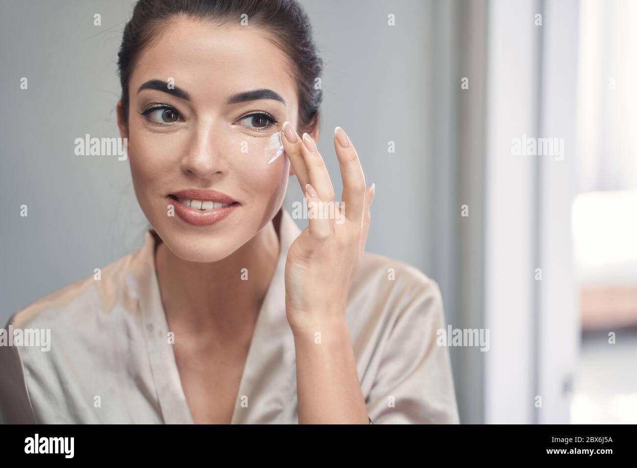 Schöne junge Brünette Anwendung Tagescreme auf ihr Gesicht Stockfoto