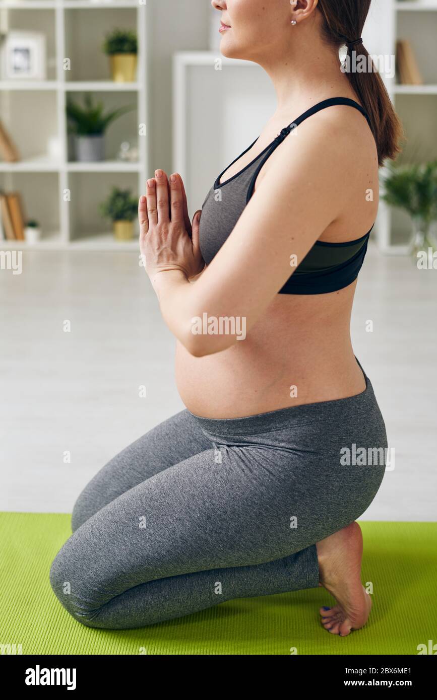 Seitenansicht der aktiven schwangeren Frau in Sportkleidung auf den Knien stehend mit ihren Händen zusammen von der Brust während Yoga-Übung Stockfoto