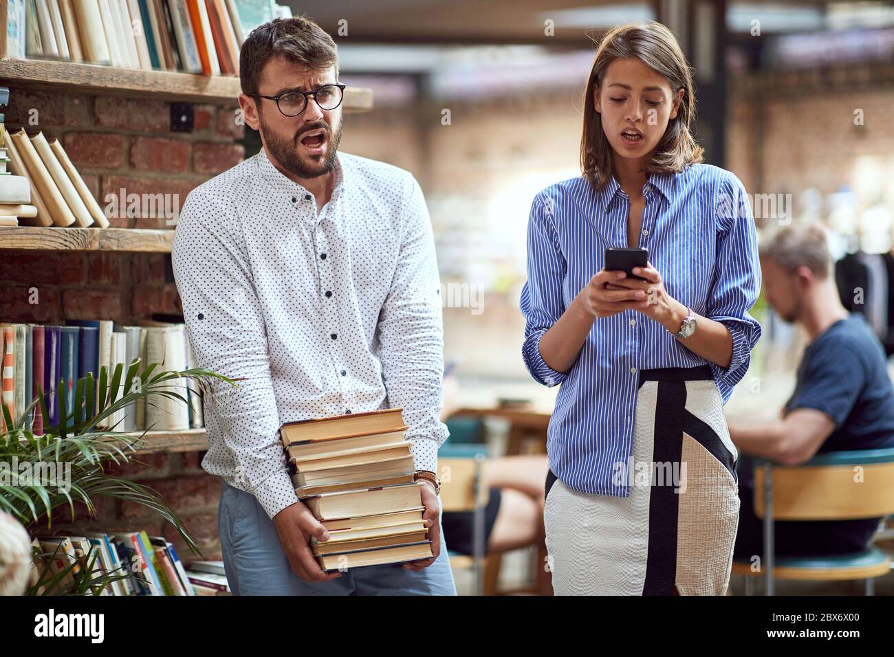 Altmodischer Mann, der schwere Bücherstapel trägt, kämpft. Moderne Frau, die E-Bücher auf ihrem Handy beobachtet. Bücher versus E-Bücher Konzept Stockfoto