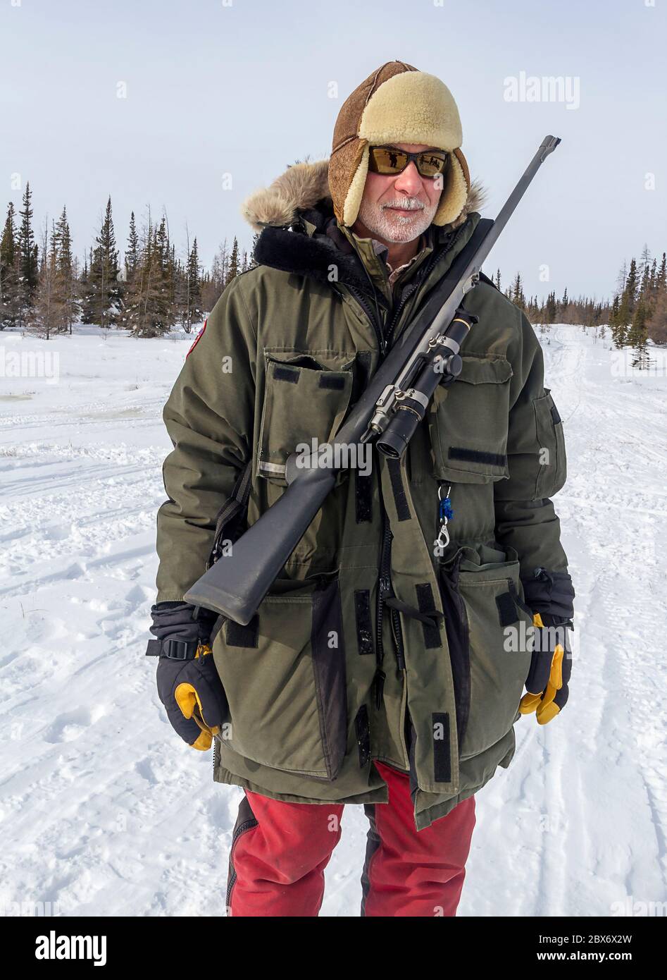 Der langjährige Churchill-Bewohner Mike Macri steht im späten Winter in der Nähe des gefrorenen Churchill River. Er trägt ein Gewehr zum Schutz gegen Eisbären Stockfoto