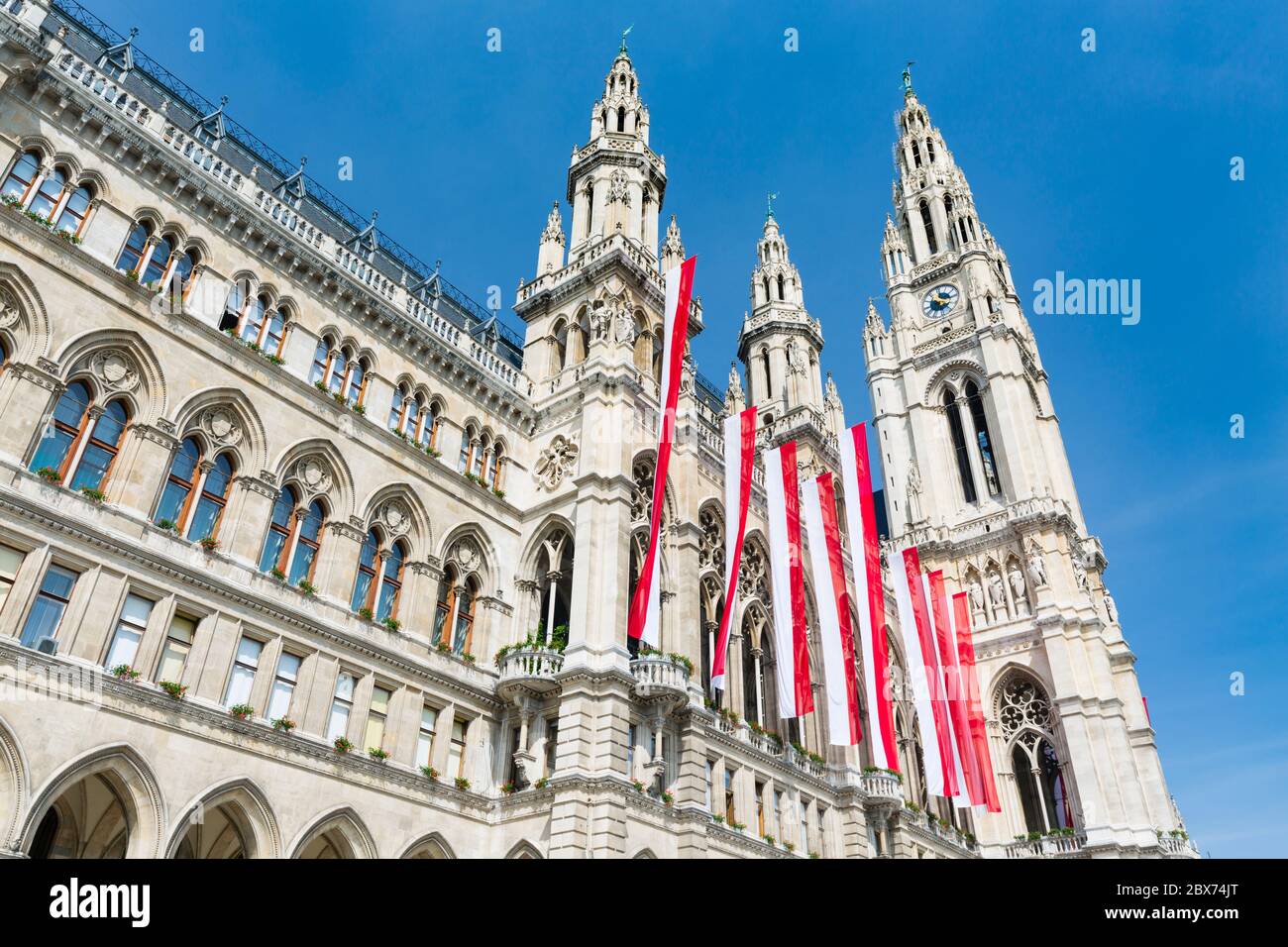 Die Vorderseite des Wiener Rathauses mit roten und weißen Fahnen und blauem Himmel, Österreich. Stockfoto