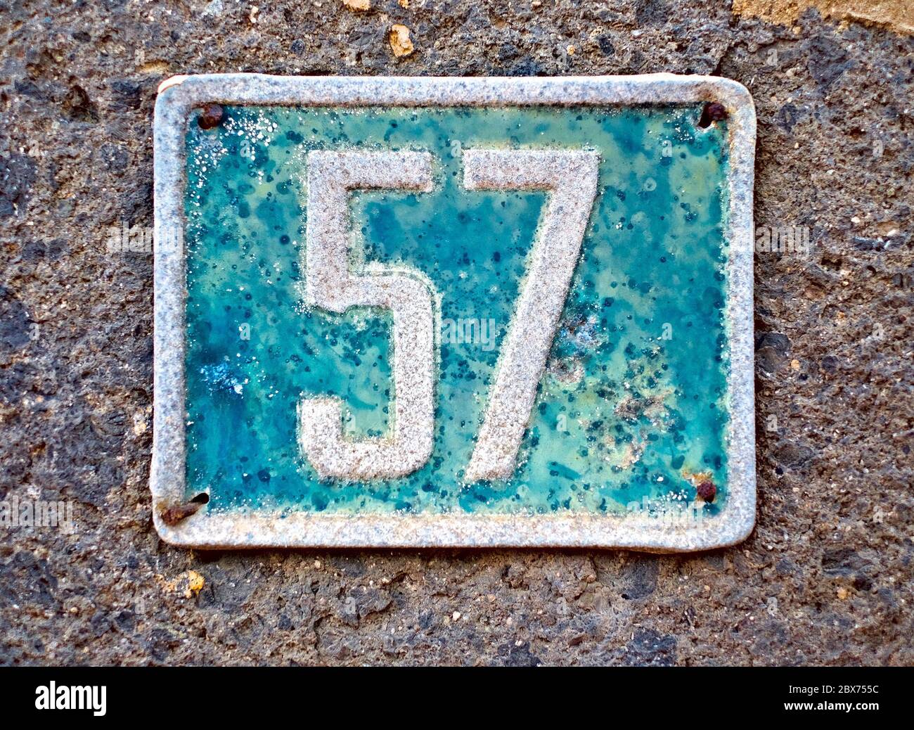 57, Nummer siebenundfünfzig, graublaues Schild mit Nummer auf einer Steinmauer. Stockfoto