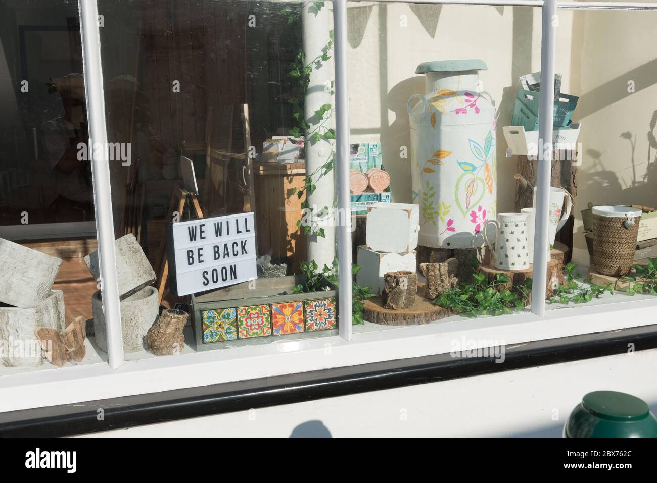 Blick auf das Schaufenster mit verschiedenen Artikeln und Schild mit der Aufschrift „Wir kommen bald wieder“. Der Shop ist während der COVID-19-Sperre vorübergehend nicht besetzt. Stockfoto