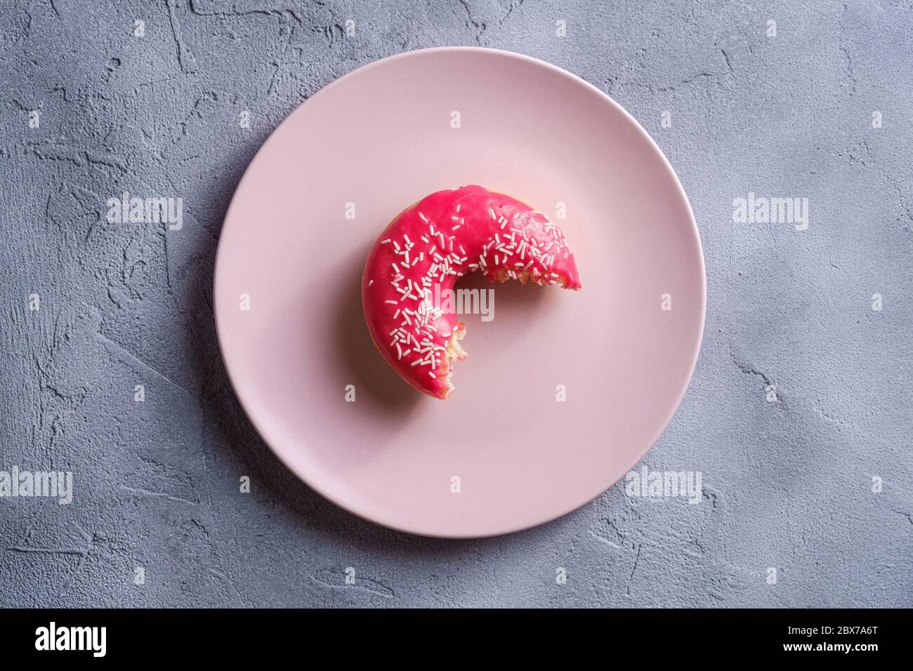 Gebissen rosa Donut mit Streuseln auf rosa Teller, süß glasierte Dessert-Food auf Beton strukturierten Hintergrund, Draufsicht Stockfoto