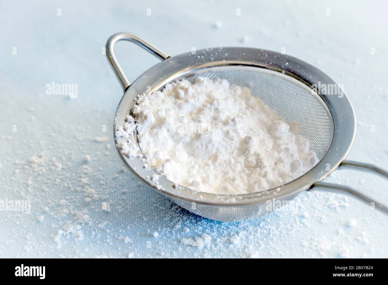 Puderzucker Zucker im Sieb. Nahaufnahme auf pastellblauem Hintergrund. Stockfoto