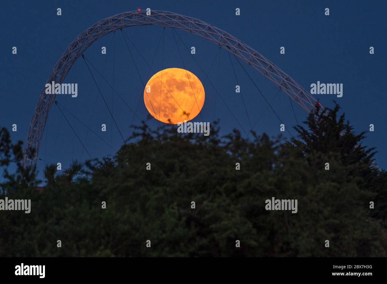 Wembley, Großbritannien. Juni 2020. UK Wetter - der Vollmond im Juni, bekannt als Erdbeermond, erhebt sich hinter dem Wembley Stadion im Nordwesten Londons. Der Vollmond im Juni war laut Almanach des alten Farmers das Signal für die Indianer der Algonquin-Stämme, wilde Erdbeeren zu ernten. Der Vollmond dieses Monats fällt auch mit einer subtilen Halbfinsternis zusammen, die auftritt, wenn die Erde einen leichten Schatten über den Mond wirft. Kredit: Stephen Chung / Alamy Live News Stockfoto