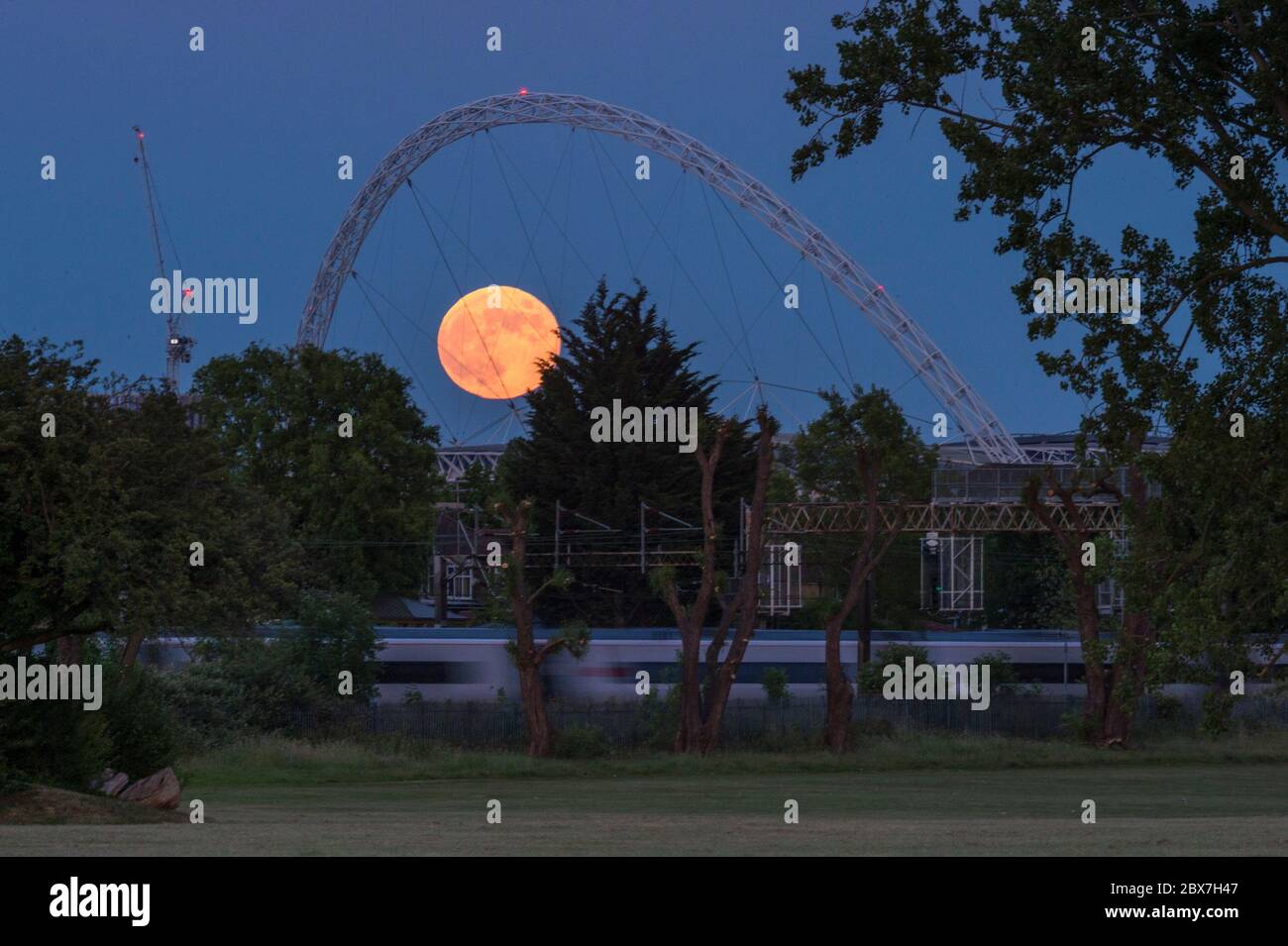 Wembley, Großbritannien. Juni 2020. UK Wetter - EIN Zug fährt vorbei, als der Vollmond im Juni, bekannt als Erdbeermond, hinter dem Wembley Stadium im Nordwesten Londons aufsteigt. Der Vollmond im Juni war laut Almanach des alten Farmers das Signal für die Indianer der Algonquin-Stämme, wilde Erdbeeren zu ernten. Der Vollmond dieses Monats fällt auch mit einer subtilen Halbfinsternis zusammen, die auftritt, wenn die Erde einen leichten Schatten über den Mond wirft. Kredit: Stephen Chung / Alamy Live News Stockfoto