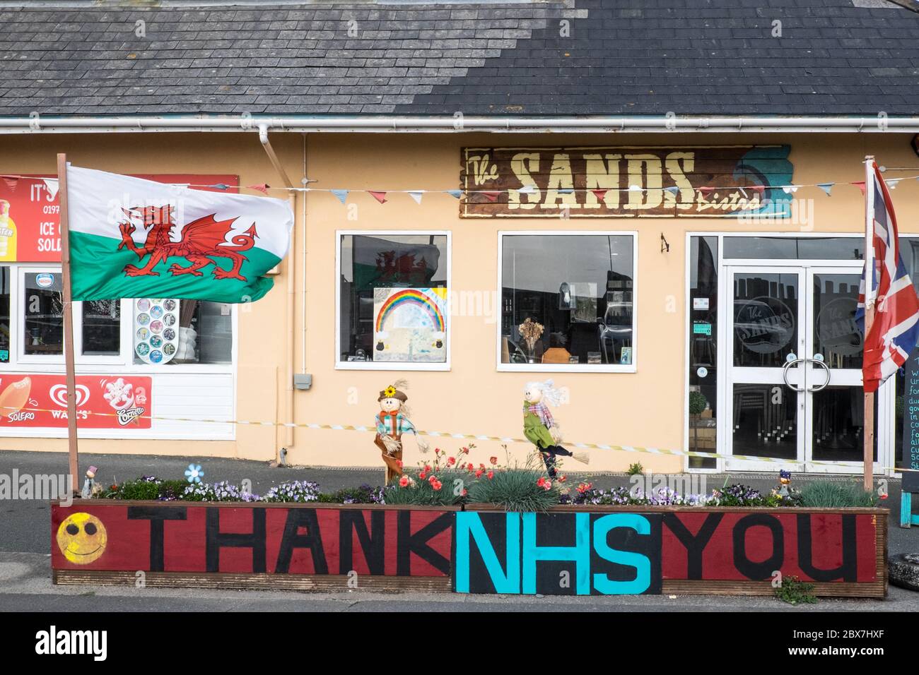 Walisische Flagge, und, Union Jack, Flagge mit Danke NHS, National Health Service, Unterstützung, Poster, Banner, von, Öffentlichkeit, Unterstützung, außerhalb, geschlossen, Sand, Café, Restaurant, dass, ist, geschlossen, aufgrund, Coronavirus, Covid 19, Pandemie, in, Borth, Meer, Urlaub, Resort, Norden, Aberystwyth, Ceredigion hat eine große Anzahl von Einheimischen und Touristen außerhalb Wales zu bleiben. Aber es hat auch eine Wirtschaft mit vielen auf Tourismus, Touristen angewiesen. Stockfoto