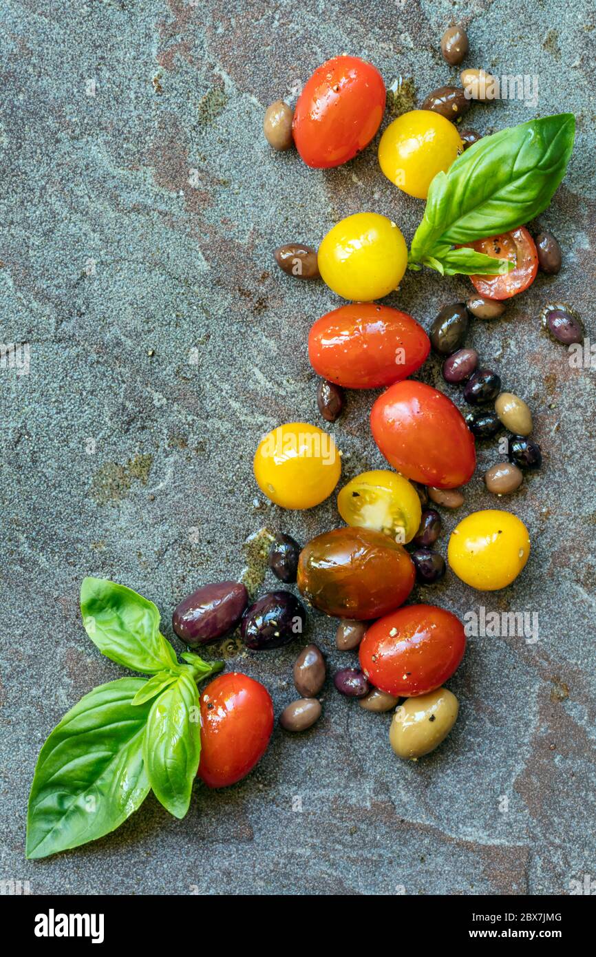 Hintergrund der Nahrung, Sorten von Erbstück Tomaten und Oliven mit Basilikum, Draufsicht über Schiefer. Stockfoto