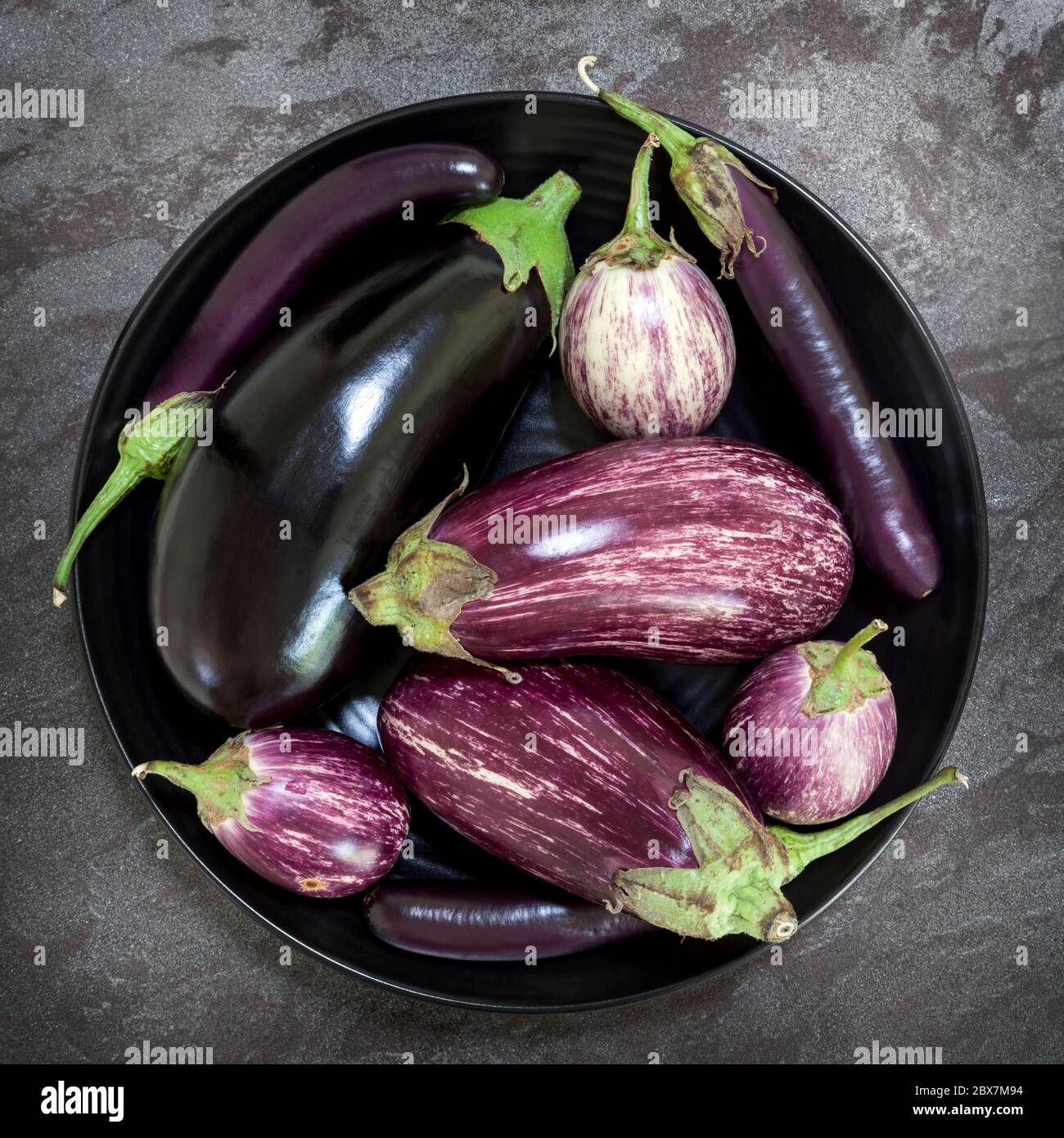 Auberginen Sorten in schwarzer Schale über dunklem Schiefer Hintergrund. Ansicht von oben. Stockfoto