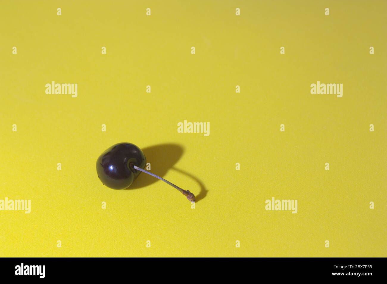 Bild einer Kirsche auf gelbem Hintergrund, die es einen minimalistischen Stil mit Platz für Texte (Kopierraum) gibt Stockfoto