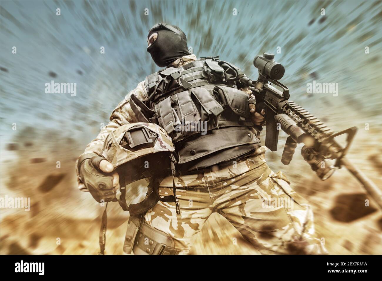 Foto eines Soldaten mit Rüstungsweste, Tarnkleidung, taktische Handschuhe, die auf dem Wüstenschlachtfeld einen Helm und ein Gewehr halten Stockfoto