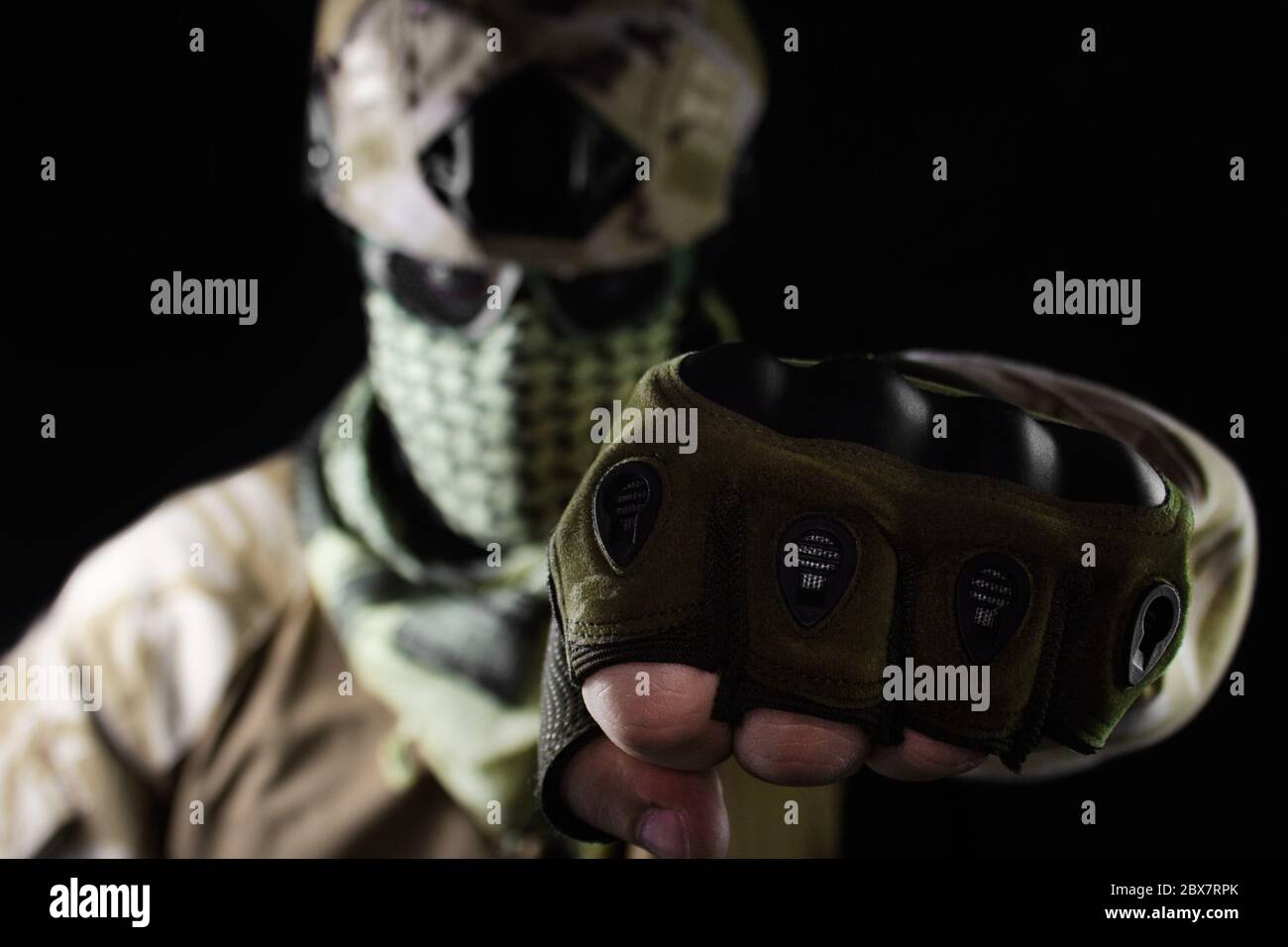 Militär Soldatenkopf mit Tarnhelm, Schutzbrille und Militär Schal Stanzen mit Faust auf schwarzem Hintergrund. Stockfoto