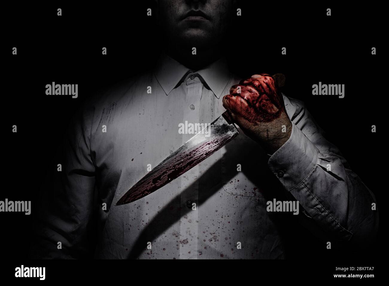 Foto eines Killers in weißem Hemd mit einem blutigen Messer auf schwarzem Hintergrund mit oberer Beleuchtung. Stockfoto