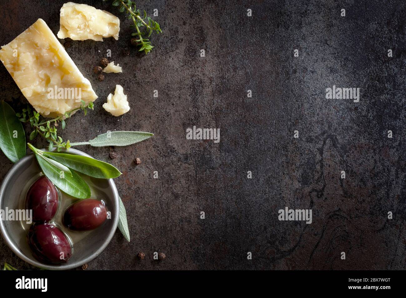 Speisehintergrund mit Parmesankäse, frischen Kräutern und Oliven, über dunklem Schiefer. Viel Kopierplatz. Stockfoto