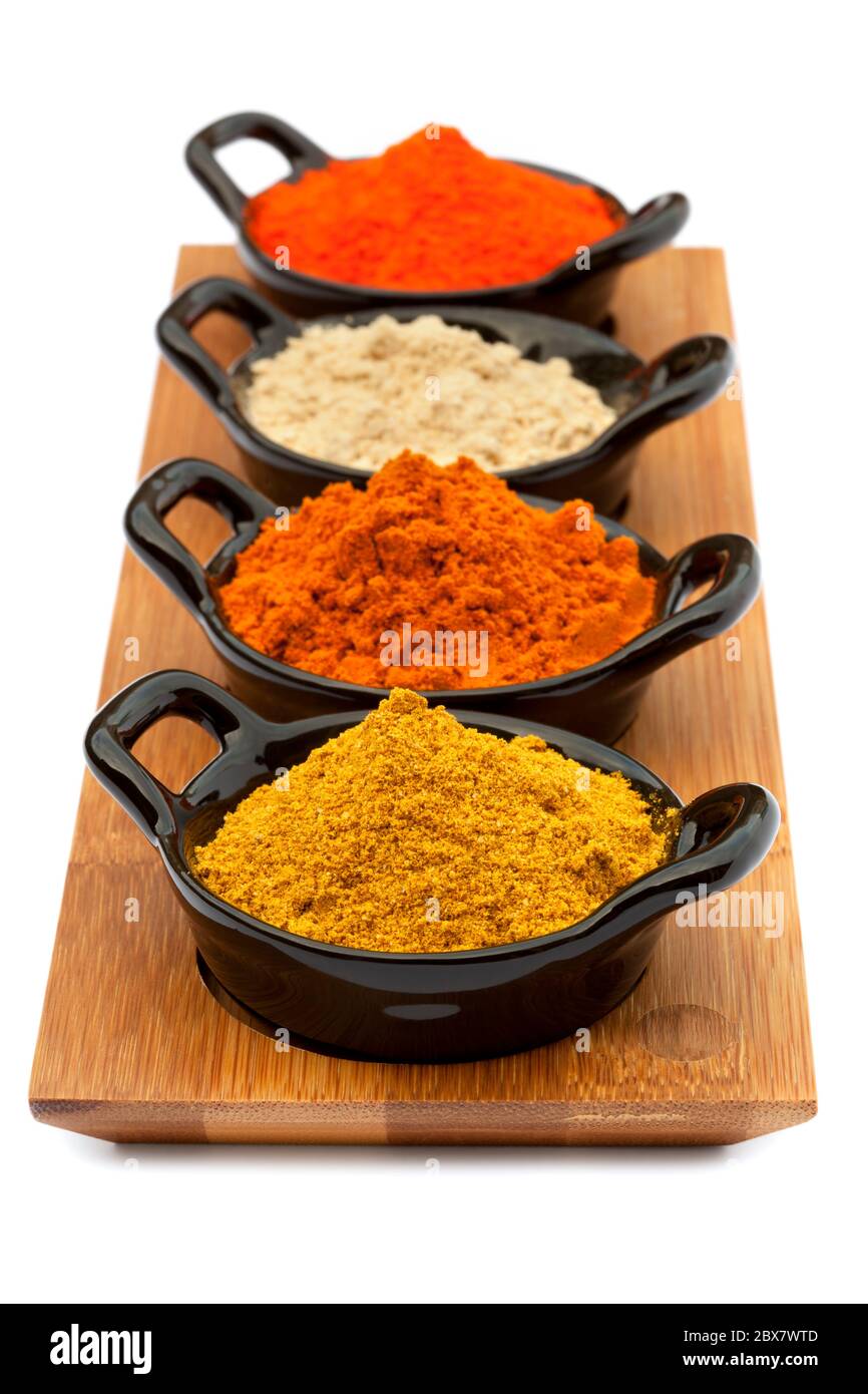 Tablett mit Gewürzen in kleinen schwarzen Schalen. Enthält Madras Currypulver, malaysisches Currypulver, gemahlener Ingwer und Safran. Stockfoto