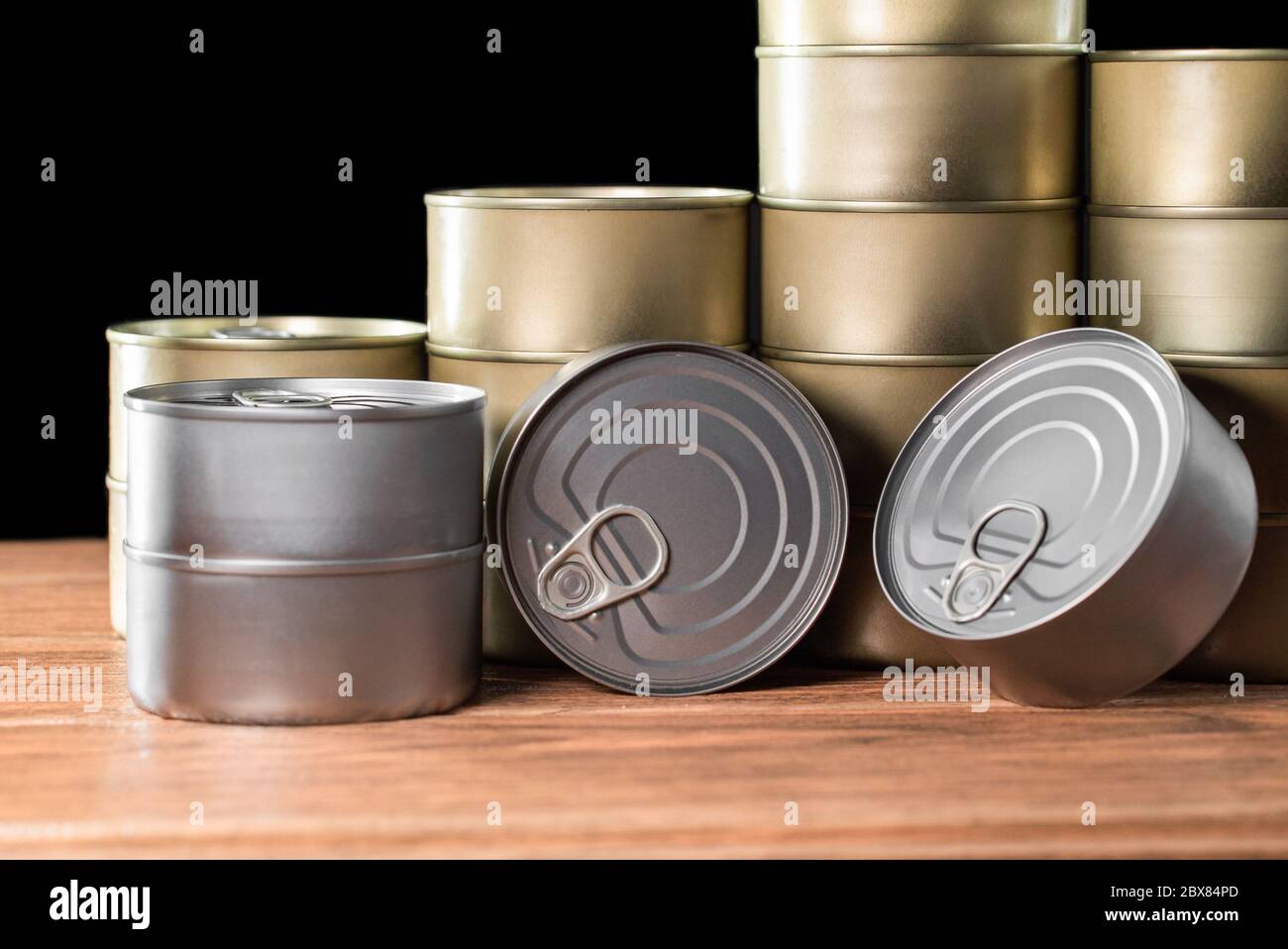 Viele Thunfischkonserven, Gold und Silber Farbe auf Holztisch und schwarzem Hintergrund Stockfoto