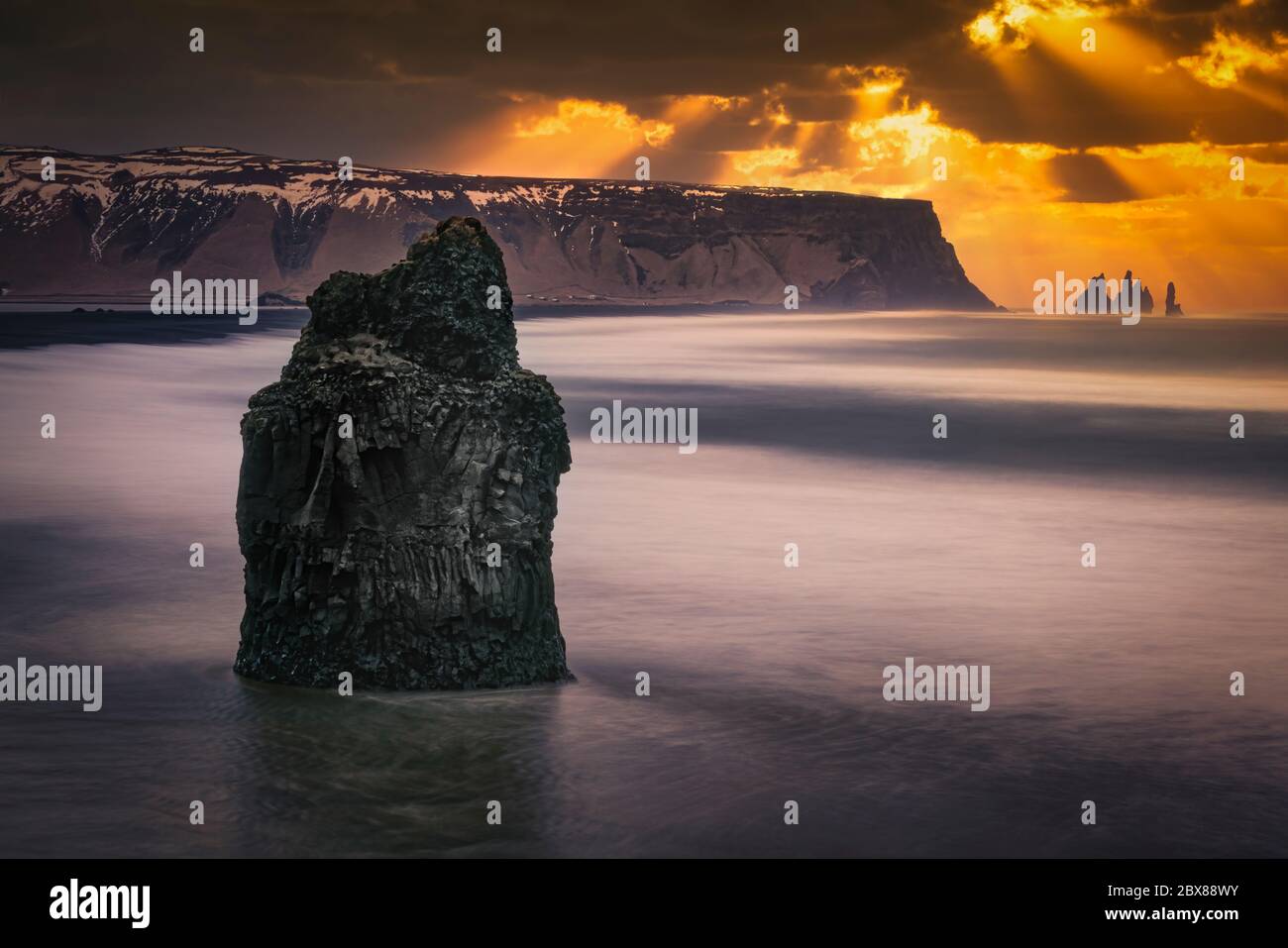 Dramatischer Himmel über Reynisfjara Strand, Island. Sonnenstrahlen, die durch die Wolken scheinen, weiße Wellen, die den schwarzen Sandstrand waschen. Stockfoto