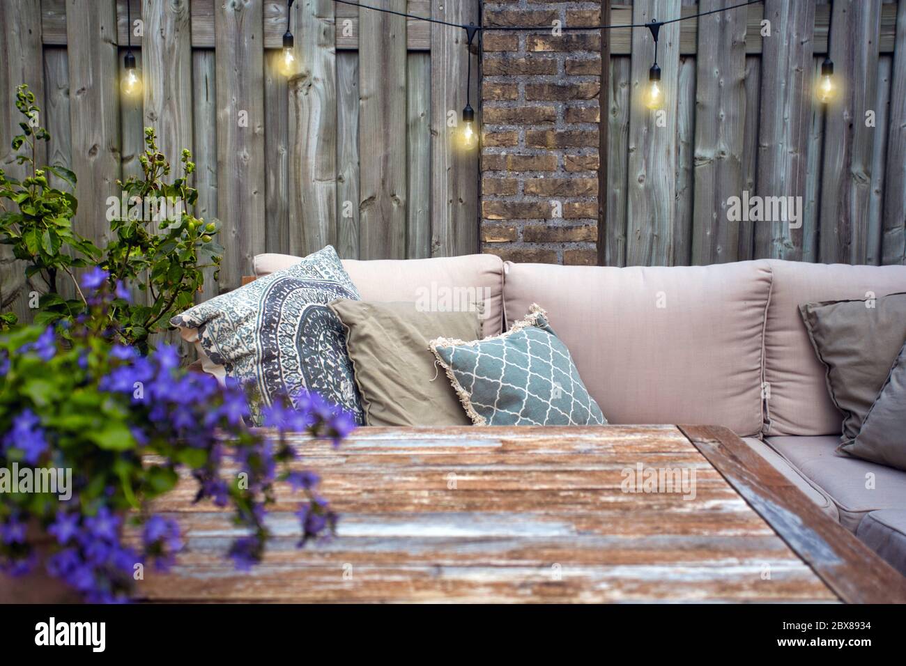 Stilvolle Gartenmöbel, Sofa mit Kissen und Lampen, Glühbirnen hängen,  gemütliche moderne Ecke auf der Terrasse Stockfotografie - Alamy