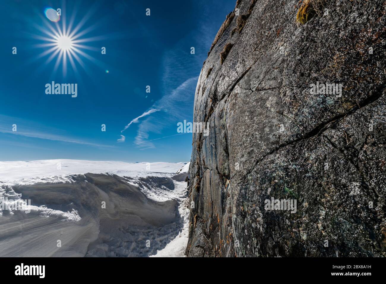 Vertikale Steinwand des Berges auf der rechten Seite werden nass im Frühling, wenn Wasser beginnt, von der Spitze nach unten zu laufen. Helle Sonne und noch viel Schnee Stockfoto