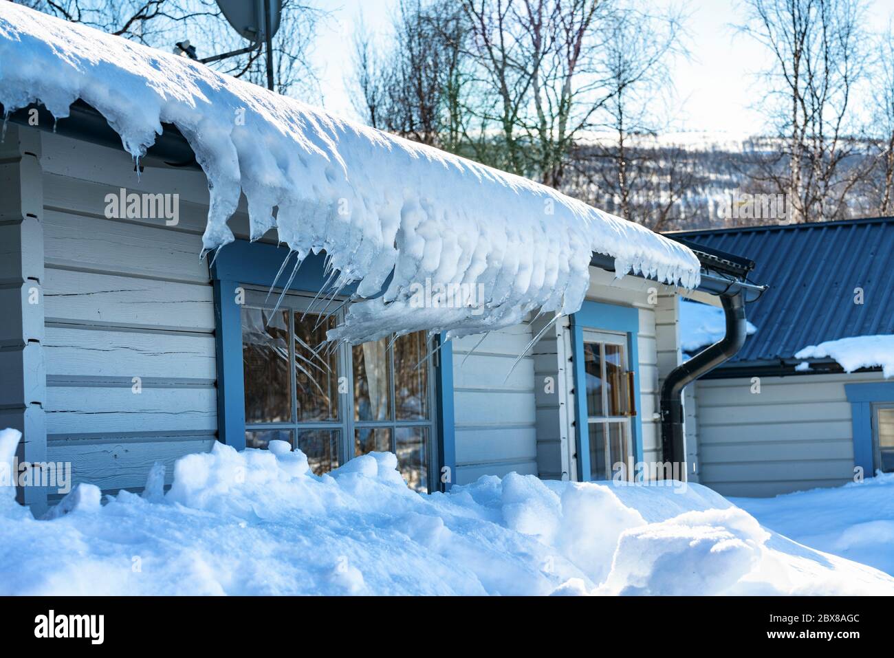 Foto von Schnee und gebogenen Eiszapfen, die vom Dach der traditionellen schwedischen Holzhütte in Lappland, Nordschweden, hängen. Stockfoto
