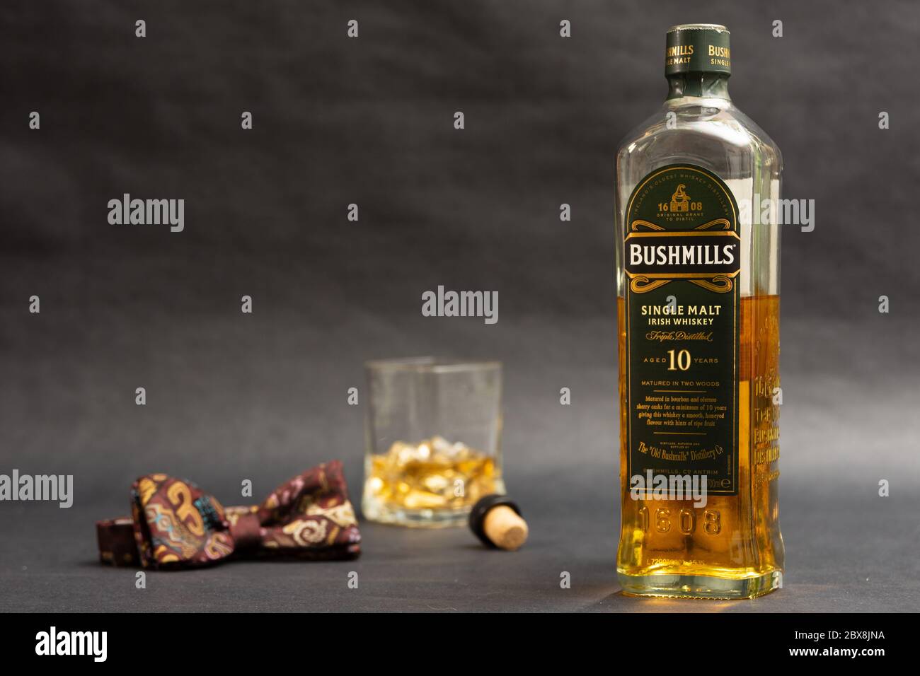 Eine Flasche Bushmills Single Paints Whiskey mit Glas und Fliege vor dunklem Hintergrund Stockfoto