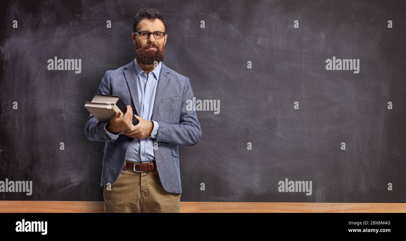 Beareded Lehrer, der Bücher hält und vor einer Tafel in einem Klassenzimmer steht Stockfoto