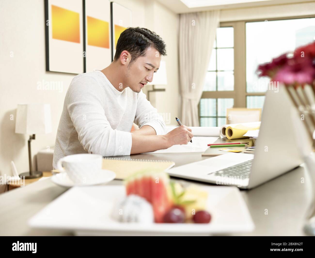 Junge asiatische Mann Design professionelle sitzen an der Küche Theke arbeiten von zu Hause (Kunstwerk im Hintergrund digital verändert) Stockfoto
