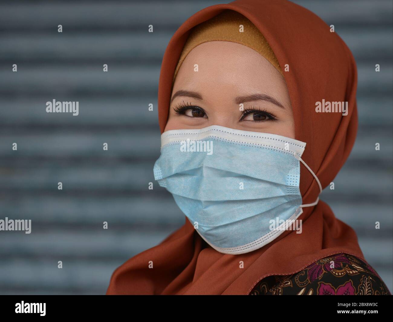Die junge malaysische Muslimah mit schönen Augen trägt während der globalen Corona-Virus-Pandemie 2019/20 eine Einweg-OP-Gesichtsmaske. Stockfoto