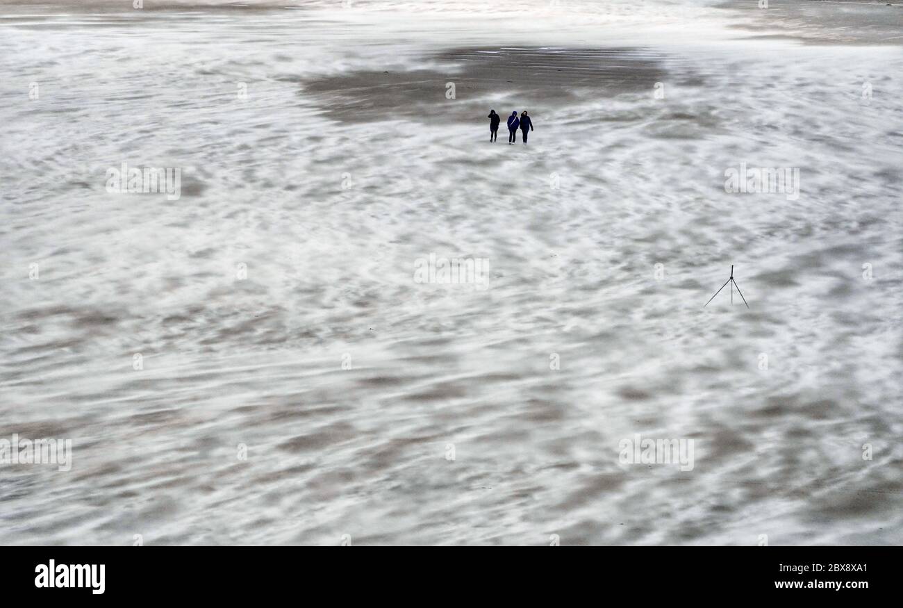 Die Menschen laufen an einem windigen Strand in Tynemouth Longsands entlang, da Großbritannien voraussichtlich am Wochenende mit starken Regenschauern, starken Stürmen und kälteren Temperaturen heimgesucht wird, wobei die Briten gewarnt werden, keine Versammlungen in den Innenbereich zu verlegen. Stockfoto