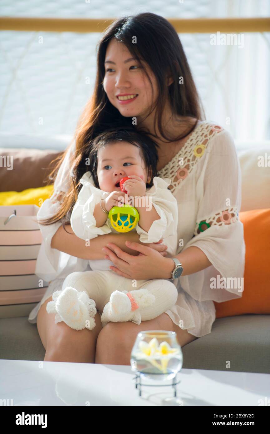 Junge glücklich und schön asiatische chinesische Frau spielen und halten süße liebenswert Baby Mädchen sitzen im Urlaub Resort genießen Sommerurlaub Reise in Stockfoto