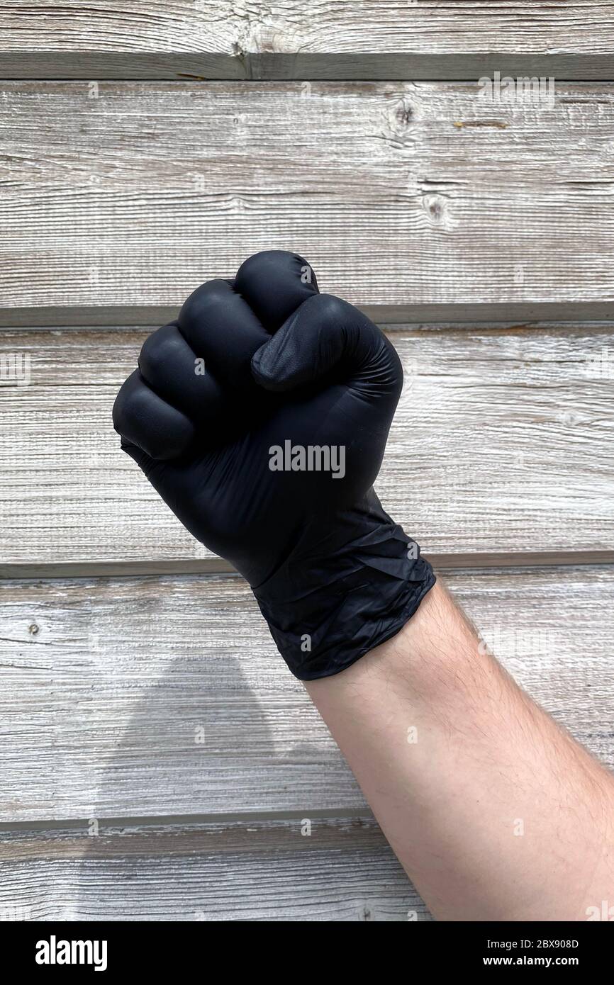 Nahaufnahme einer Handfäuste mit schwarzen medizinischen Schutzhandschuhen auf Holzhintergrund, Black Lifes Matter Konzept Stockfoto