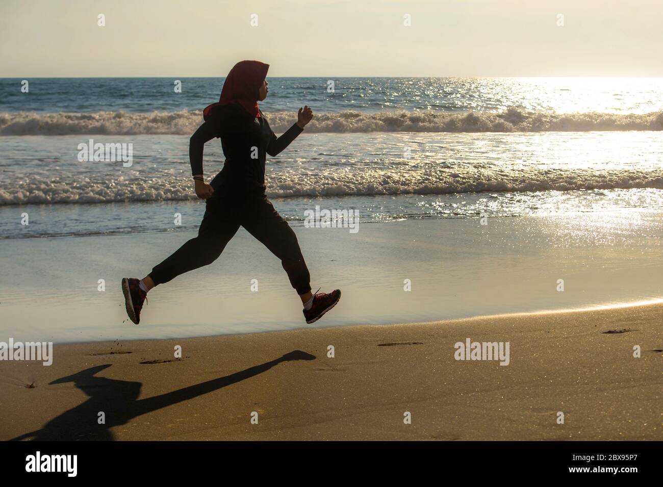 Junge gesunde und aktive Läufer muslimische Frau im Islam hijab Kopftuch Laufen und Joggen am Strand tragen traditionelle arabische Sportkleidung in fitn Stockfoto