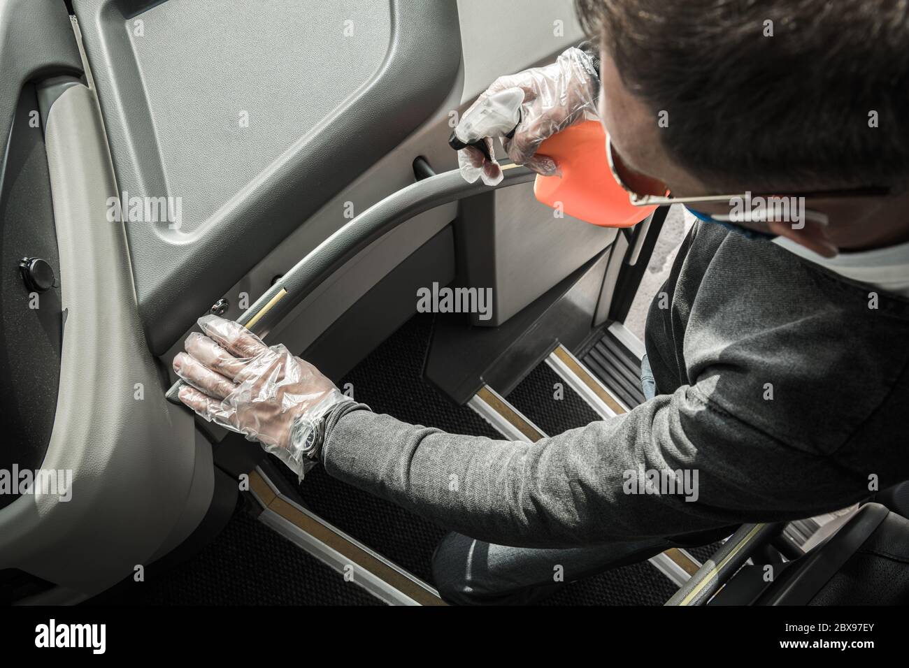 Kaukasischer Intercity-Busfahrer, der Geländer mit Alkohol in Spray desinfiziert. Vorbereitung Moto Coach für eine weitere Reise des Tages. Stockfoto