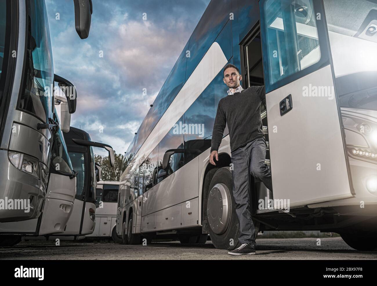 Zufrieden kaukasischen Busfahrer in seinen 30ern verlassen Coach nach harten Tag auf der Straße. Öffentliche Verkehrsmittel. Am Frühen Abend Sommerstunden. Bus D Stockfoto