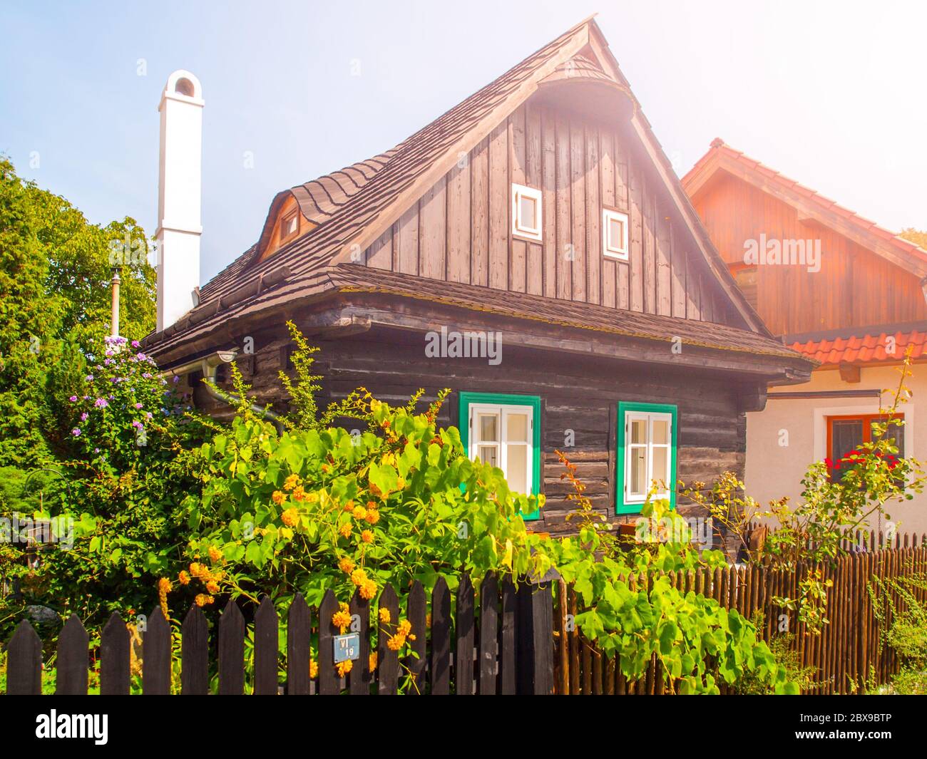 Altes traditionelles Fachwerkhaus mit romantischem und idyllischem üppigen grünen Blumengarten mit Holzzaun an sonnigen Sommertagen. Mährische ländliche Architektur. Stockfoto