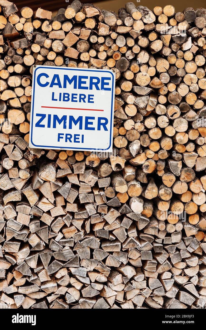 Zimmer in italienischer und deutscher Sprache verfügbar (Camere libere und Zimmer frei). Werbeschild hängt auf einem Stapel Feuerholz Stockfoto